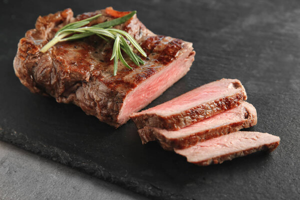 Slate plate with tasty grilled steak on grey background