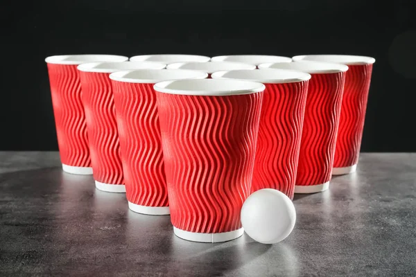 Cups and ball for beer pong on table against dark background