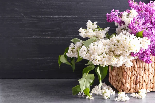 Wicker box with beautiful blossoming lilac on table against wooden background