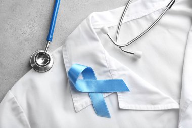 Blue ribbon, stethoscope and white coat on light background, closeup. Prostate cancer concept clipart