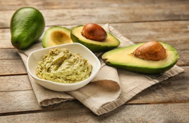 Lezzetli guacamole ve ahşap masa üzerinde olgunlaşmış avokado ile kase