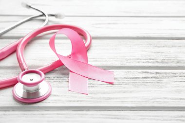 Ahşap arka planda pembe kurdele ve steteskop, yakın plan. Göğüs kanseri farkındalığı konsepti