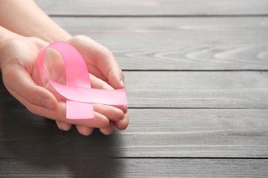 Pembe kurdele ahşap arka plan üzerinde tutan eller. Meme kanseri bilinçlendirme kavramı