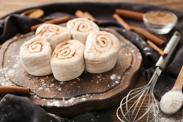 Wooden board with uncooked cinnamon rolls on kitchen table