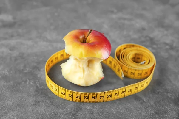 Bitten apple and measuring tape on table. Diet food