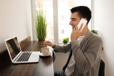 Kafede dizüstü bilgisayar kullanırken telefonda konuşurken genç serbest meslek