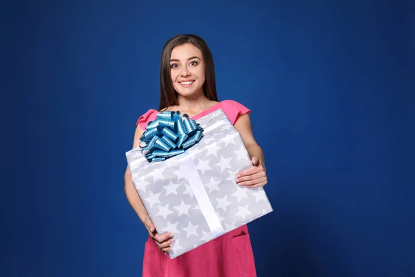 Beautiful young woman with big gift box on color background