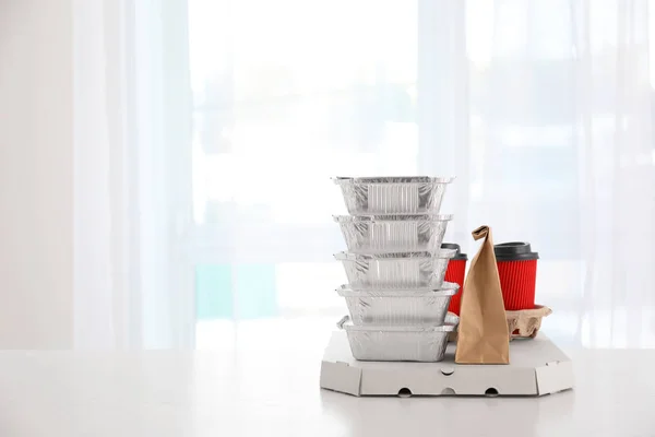Paper package, foil containers and coffee cups on table against light background. Food delivery