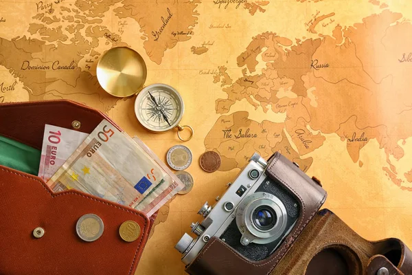 Photo camera, compass and money on vintage world map. Travel planning concept