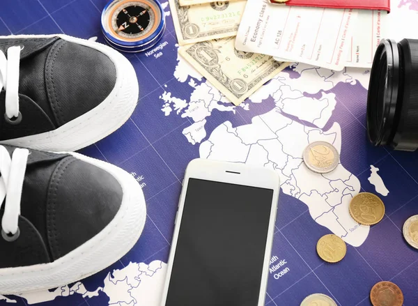 Male shoes, mobile phone, money and compass on world map. Travel planning concept