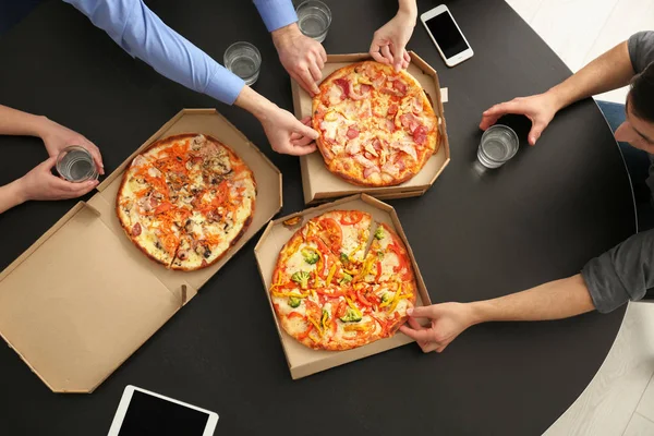 Young people eating pizza at table in office