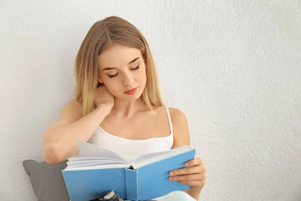 Young woman reading book near light wall