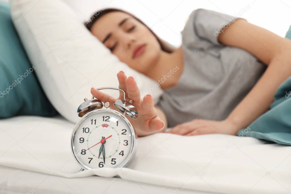 Young woman with alarm clock on bed in morning