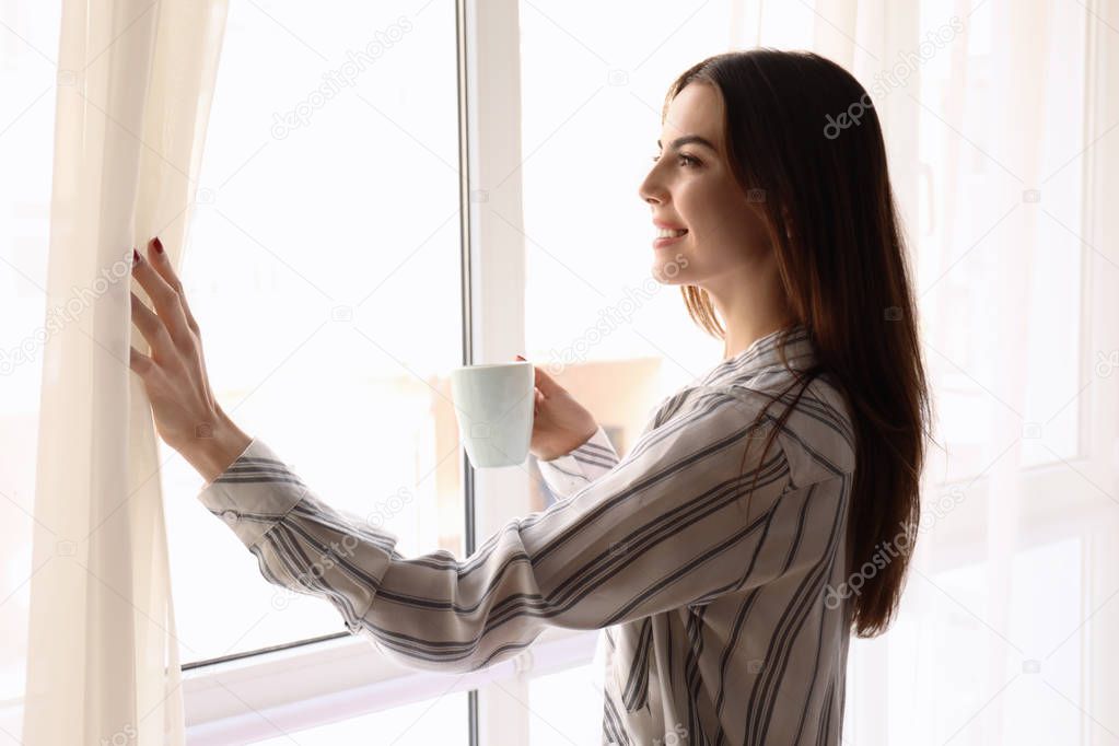 Morning of beautiful young woman with cup of coffee near window