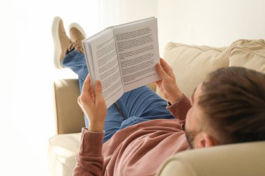 Genç adam evde koltukta yalan kitap okuma