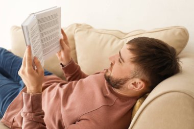 Genç adam evde koltukta yalan kitap okuma