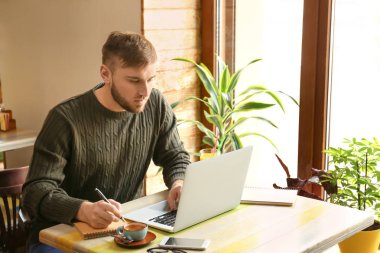 Dizüstü bilgisayar ve notebook kafede çalışan genç serbest meslek