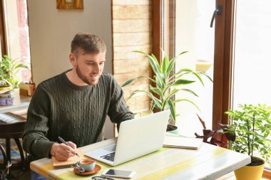 Dizüstü bilgisayar ve notebook kafede çalışan genç serbest meslek