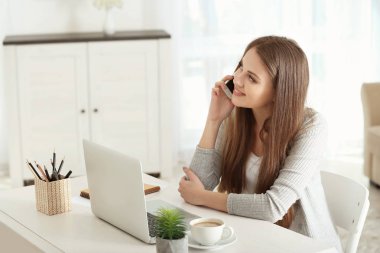 Ev ofis içinde laptop üzerinde çalışırken telefonla konuşan kadın serbest meslek