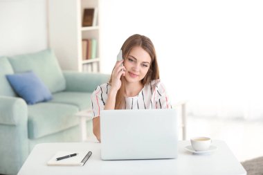 Ev ofis içinde laptop üzerinde çalışırken telefonla konuşan kadın serbest meslek