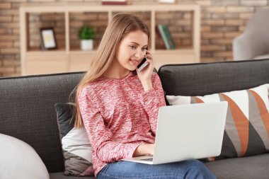 Evde dizüstü bilgisayarda çalışırken telefonla konuşan kadın serbest meslek