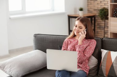Evde dizüstü bilgisayarda çalışırken telefonla konuşan kadın serbest meslek
