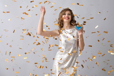 İçki ve gri arka plan üzerine düşen konfeti ile güzel genç kadın