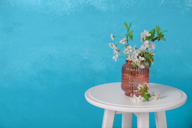 Masanın üzerinde renk arkaplanına karşı çiçek açan güzel dalları olan vazo