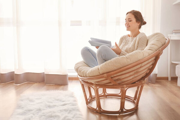Young woman reading book on lounge chair at home