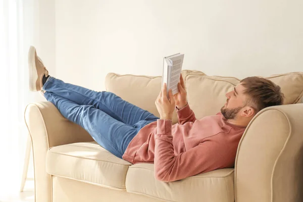 Jovem Homem Lendo Livro Enquanto Deitado Sofá Casa — Fotografia de Stock