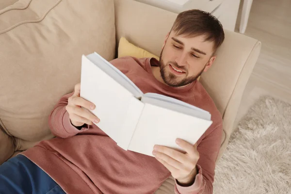 Jovem Homem Lendo Livro Enquanto Deitado Sofá Casa — Fotografia de Stock