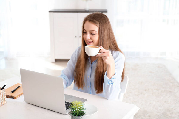 Female freelancer drinking coffee while working on laptop in home office