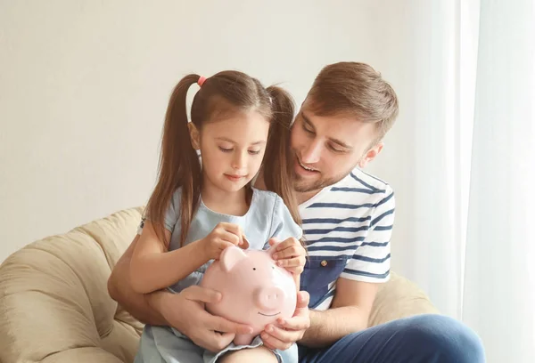 Niña Feliz Con Padre Sentado Sillón Poniendo Moneda Alcancía Interior —  Fotos de Stock