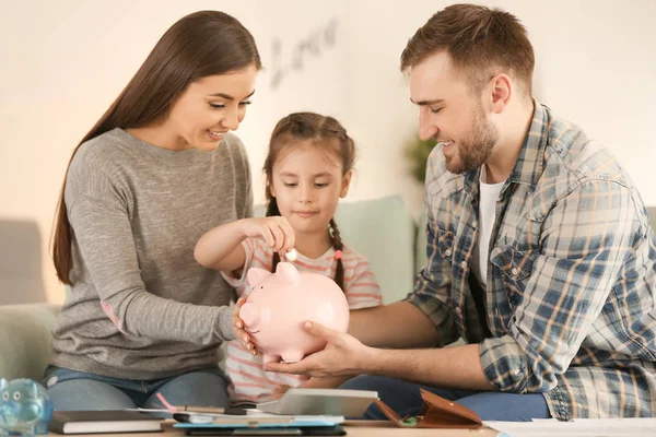 小女孩和她的父母坐在沙发上 把硬币放进存钱罐的室内 货币储蓄概念 — 图库照片