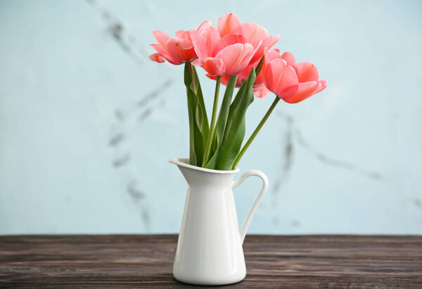 Vase with beautiful tulips on table against light background