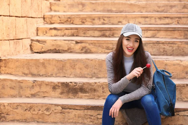 Attractive young woman with lollipop sitting on steps outdoors