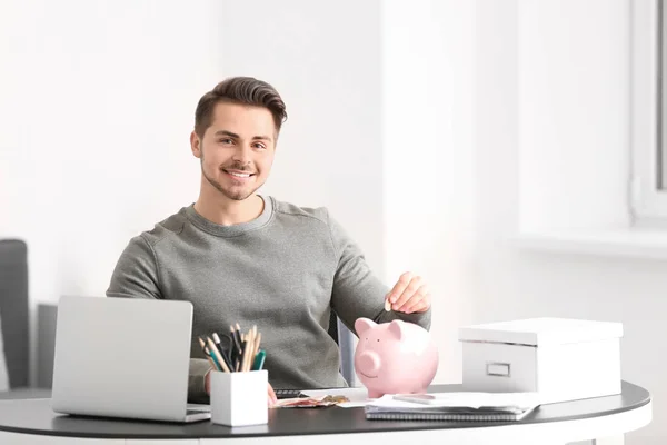Man putting coin into piggy bank indoors. Money savings concept