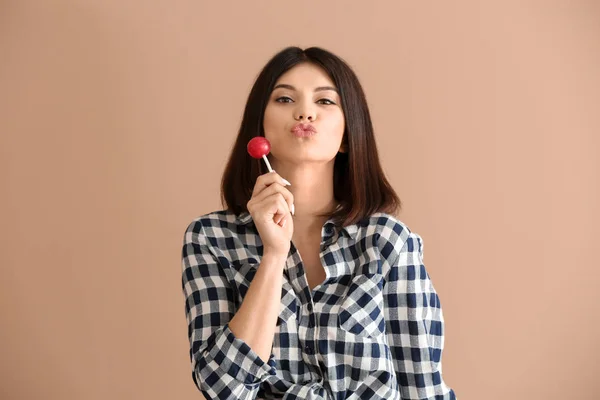 Beautiful young woman with lollipop on color background