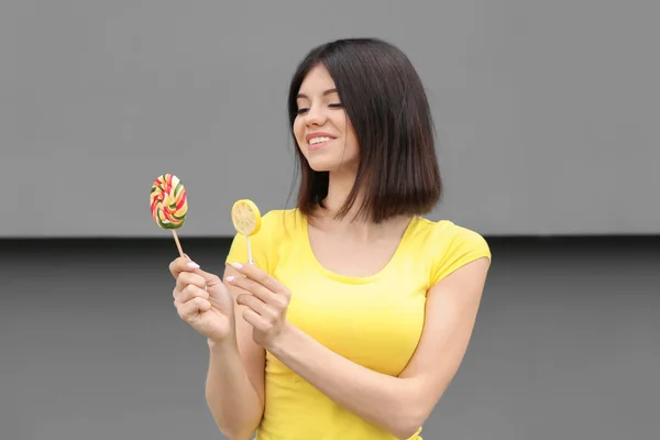 Beautiful young woman with lollipops on grey background