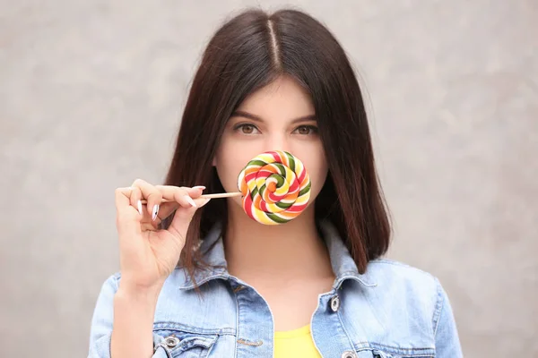 Beautiful young woman with lollipop on grey background