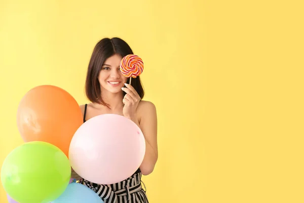 Beautiful young woman with lollipop and balloons on color background