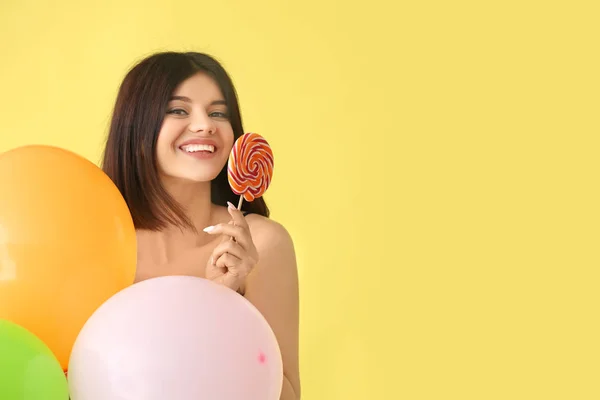 Beautiful young woman with lollipop and balloons on color background