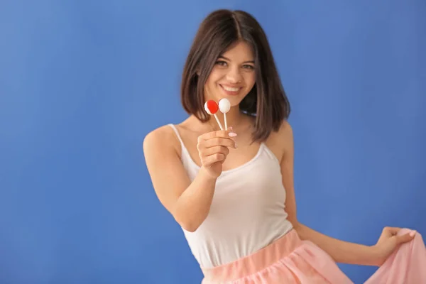 Beautiful young woman with lollipops on color background