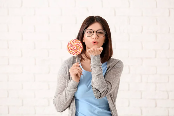 Beautiful young woman with lollipop blowing kiss on light background