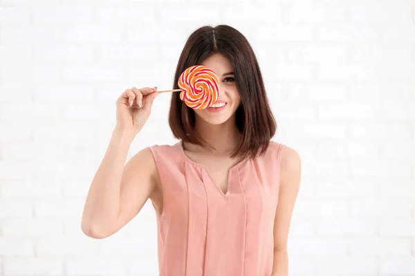Beautiful young woman with lollipop on light background