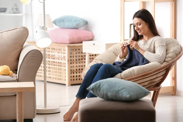 若い女性の肘掛け椅子に座っていると屋内で暖かいセーターを編む — ストック写真