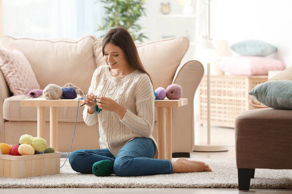Young woman knitting warm sweater indoors