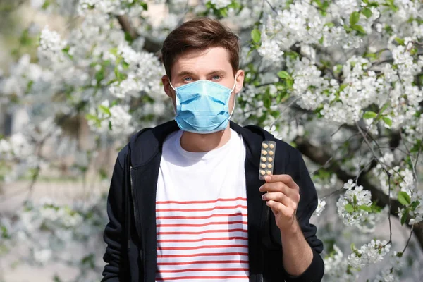 Jovem Máscara Protetora Segurando Pílulas Perto Árvore Florescente Conceito Alergia — Fotografia de Stock