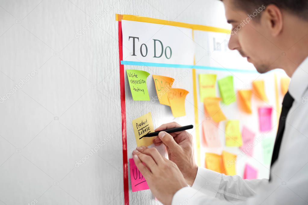 Man writing on sticky note attached to scrum task board in office