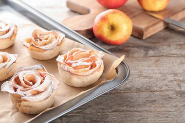 Ahşap masa üzerinde lezzetli gül şekilli elma pasta ile fırın tepsisi